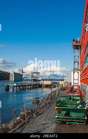 Construction of a commercial building near water.  Workmen are visible.  Pallets of green-hued glass for the building are in the image. Stock Photo