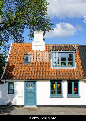 A small white romantic historical house with a clay tile roof and a white chimney against a blue sky with white clouds background Stock Photo