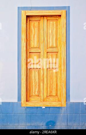 Tall wooden frame closed window with varnished shutters in a blue wall. Stock Photo