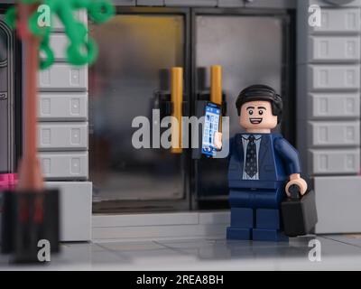 Tambov, Russian Federation - July 26, 2023 A Lego businessman minifigure standing in front of the doors of a bank and answering the cellphone. Stock Photo