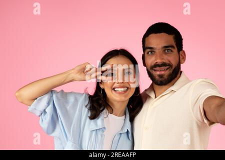 Happy loving young couple have fun on pink, taking selfie Stock Photo