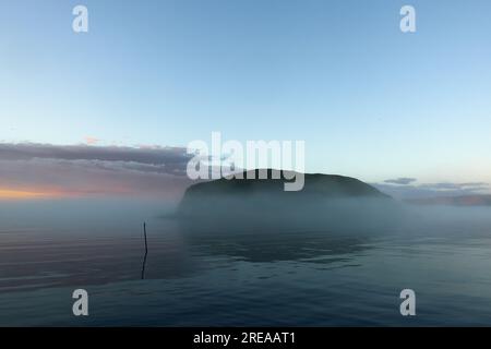 Small island of Lille Kamøya late on an August evening just outside Kamøyvær fishing village with midnight sun and sea fog. Stock Photo