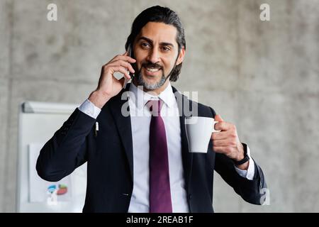 Cheerful attractive manager talking on phone, drinking coffee Stock Photo