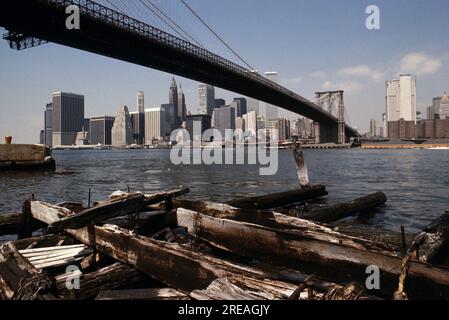 AJAXNETPHOTO. JULY 1975. NEW YORK, USA. - EAST RIVER CROSSING - BROOKLYN BRIDGE SPANNING THE EAST RIVER FROM THE BROOKLYN SIDE TOWARDS LOWER MANHATTAN, OLD WOODEN PIER SUPPORTS IN FORE. PHOTO:JONATHAN EASTLAND/AJAX REF:601886 139 Stock Photo