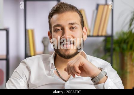 Portrait of happy smiling bearded middle eastern businessman at modern home office workplace desk looking at camera. Male in formal shirt. Man guy remote distant online working on laptop Stock Photo