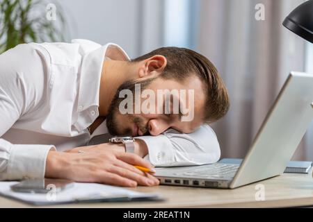 Bored sleepy middle eastern businessman worker working on laptop computer, leaning on hand falling asleep at office. Exhausted tired freelancer workaholic lebanese man. Employment, occupation workless Stock Photo