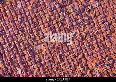 Chequered pattern of repetitive small squares on old rusty metal plate in beautiful warm sunset light. Stock Photo