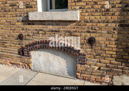 Full frame texture background of an attractive old mottled yellow and brown color brick wall, with view of an enclosed arched basement window Stock Photo