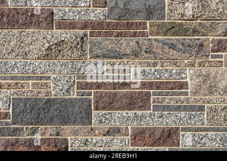 Full frame texture background of a modern granite stone wall in ashlar masonry style, in varying sizes and shades of white, brown, red and blue Stock Photo