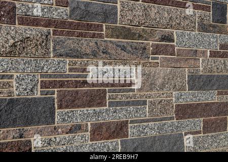 Full frame texture background of a modern granite stone wall in ashlar masonry style, in varying sizes and shades of white, brown, red and blue Stock Photo