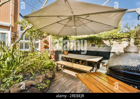 a patio with an umbrella over the table and grill in the back yard, on a sunny day photo taken from behind Stock Photo