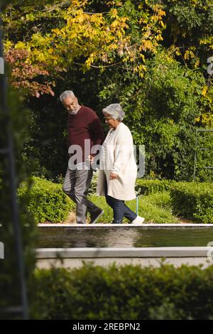 Happy senior biracial couple holding hands and walking in garden at home Stock Photo