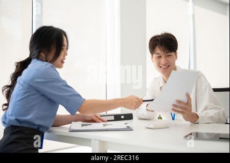Two professional young Asian office workers are discussing work, planning a project, and examining reports in the office together. Stock Photo