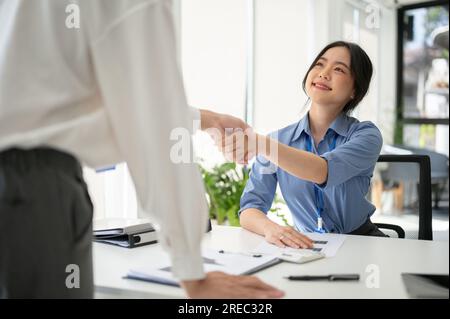 A beautiful and friendly Asian female HR recruiter is shaking hands with a candidate after an interview in the office. job interview, meeting, welcome Stock Photo