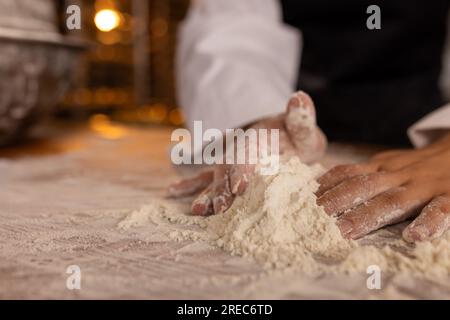 Asian female baker working in bakery kitchen, kneading dough, copy space Stock Photo