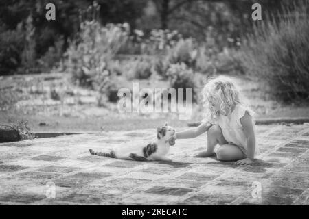 A little blonde girl stroking a cat in summer sunshine Stock Photo