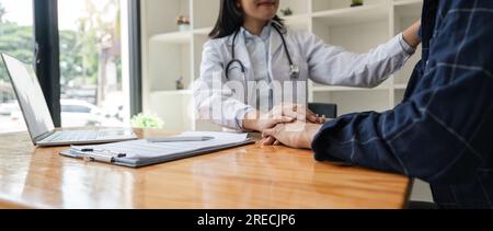Asian man visiting doctor, getting optimistic news after medical checkup, therapy. Young asian woman doctor holding hand of patient, giving hope Stock Photo