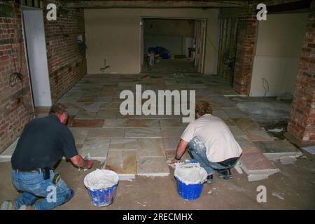 Two workmen laying large floor tiles (perhaps flagstones) as part of a conversion at the rear of The Crown Hotel in Framlingham a Suffolk market town. Stock Photo
