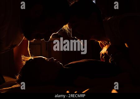 Dark silhouette of mother and father, who leaned over baby at night. Care and protection of newborn. Strong, happy family. Concept of parenthood. Lovi Stock Photo