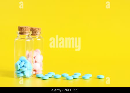 Vitamin B complex, tablets, dietary supplement. A set of blue and pink pills in glass bottles on a yellow background. Health care, painkillers and med Stock Photo