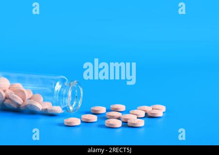 Pink pills are poured out of a glass bottle on a blue background. Vitamin B complex, copy space. Health care, medical pills and dietary supplements Stock Photo