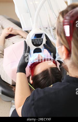 Close-up portrait of a female patient at dentist in the clinic. Teeth whitening procedure with ultraviolet light UV lamp. Stock Photo