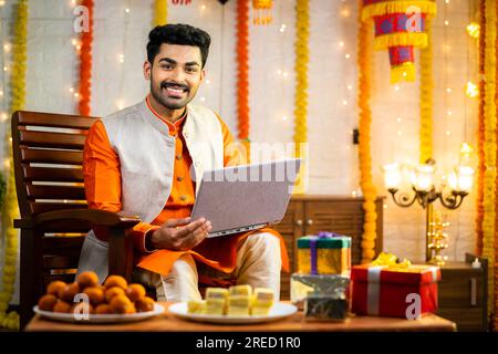 happy young man using laptop during diwali festival celebration at decorated home by looking at camera Stock Photo