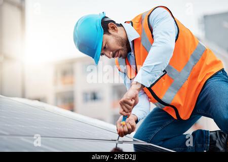 Solar panels, tool and male engineer on a rooftop doing maintenance or repairs with screwdriver. Renovation, handyman and zoom of an industrial worker Stock Photo