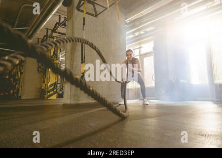 Muscular fitness woman trains triceps with two cables by her hands on background of fitness center Stock Photo