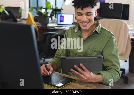 Happy biracial man holding a digital tablet using graphic tablet at office Stock Photo
