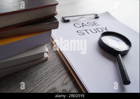 Paper clipboard with text CASE STUDY, magnifying glass and books on table. Stock Photo