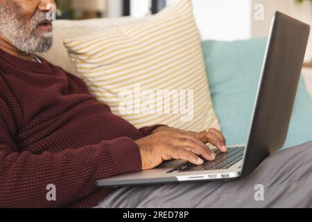 Senior biracial man sitting on couch using laptop at home Stock Photo