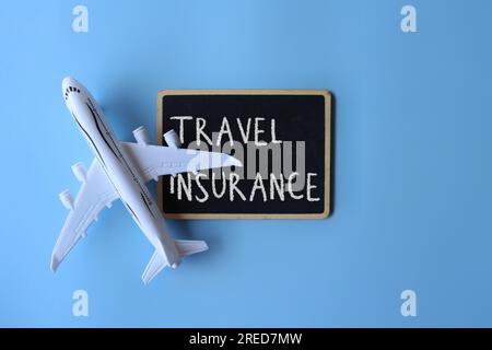 Top view image of toy plane and chalkboard with text TRAVEL INSURANCE on blue background. Stock Photo