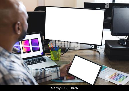 Indian male designer using tablet and computer with copy space on screens at desk in office Stock Photo
