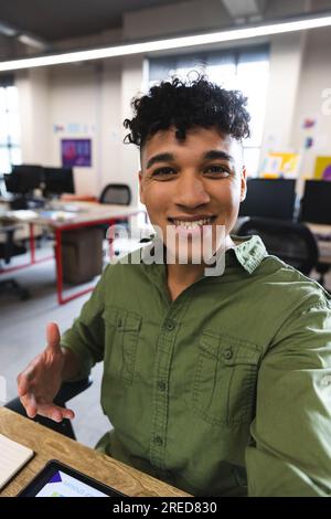 Biracial man smiling looking at the camera on smartphone during a video call at office Stock Photo
