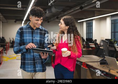 Busy diverse male and female colleagues using tablet and talking standing in office Stock Photo