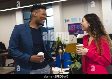 Happy diverse male and female colleagues having coffee and talking standing in office Stock Photo