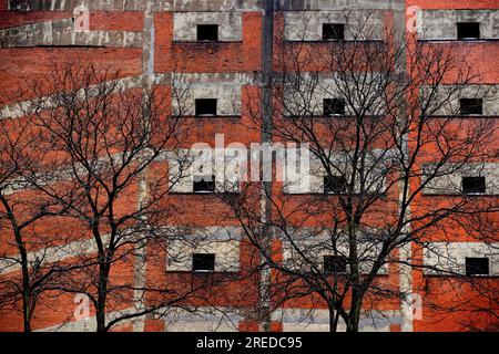Contrasting image of leafless tree branches in front of  a multi level brick parking garage. Stock Photo