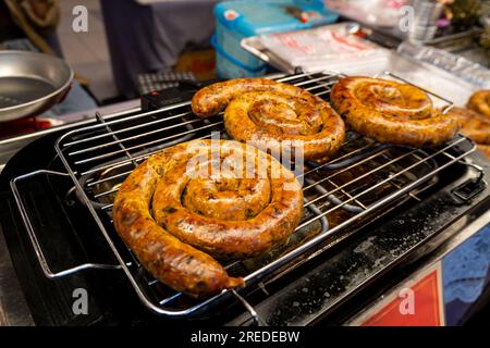Grilled sausages on grill with smoke and flame on dark background Stock Photo
