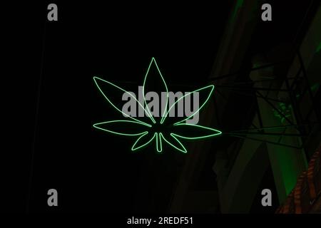 Neon sign on a brick wall in the shape of a simplified weed leaf. Stock Photo