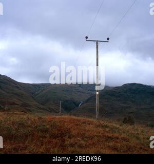 A telegraph pole stands in a Scottish heather landscape with the wire leading up to a cloudy mountain top Stock Photo