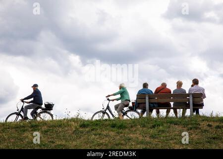 seniors sitting on a bench on the dike in Zons on the river Rhine, bicycle driver, North Rhine-Westphalia, Germany Senioren sitzen auf einer Bank auf Stock Photo