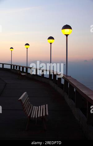 Empty white wooden seat and spherical yellow street lamps on El Morro headland at sunset, Arica, Chile Stock Photo