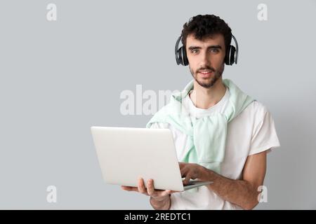 Young man in headphones working with laptop on light background Stock Photo