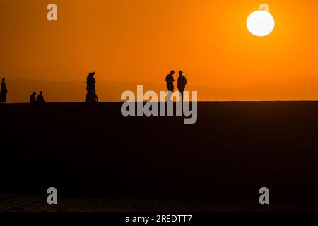 Silhouette of tourists watching the sun set behind a distant mountain in summer Stock Photo