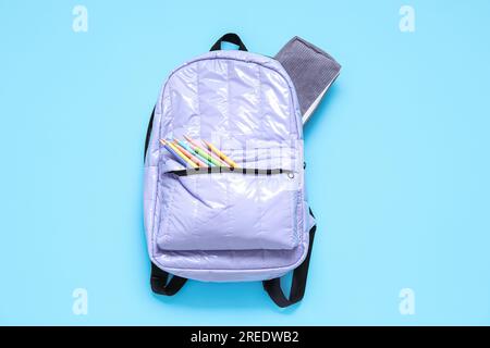 Lilac school backpack with stationery on blue background Stock Photo