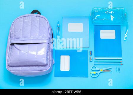 Lilac school backpack with stationery on blue background Stock Photo