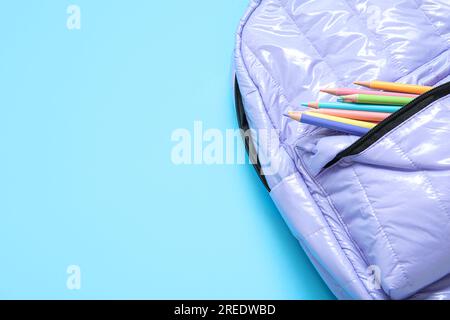Lilac school backpack with stationery on blue background Stock Photo
