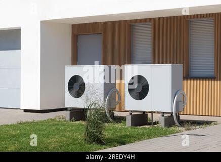 Two eco-friendly air source heat pumps situated in front of a modern house with a lush lawn, symbolizing green heating solutions. Stock Photo