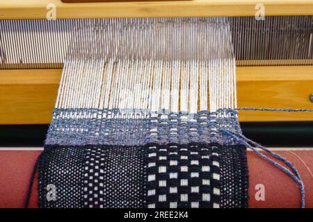 Close-up of a floor loom with black white and blue hand-woven textiles Stock Photo